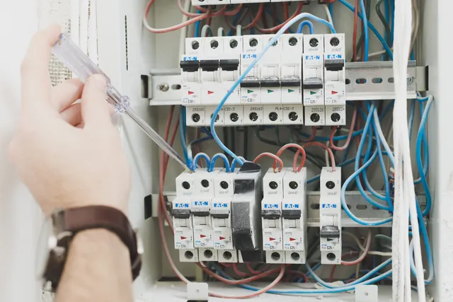 Elektrikář v červených rukavicích pracuje na zapojení rozvaděče